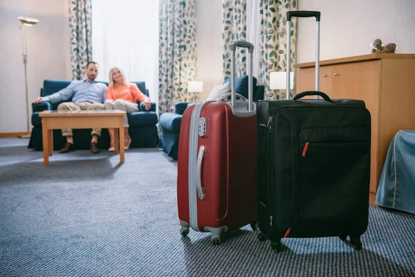 Close-up view of two suitcases and mature couple sitting on sofa in hotel room — Stock Photo
