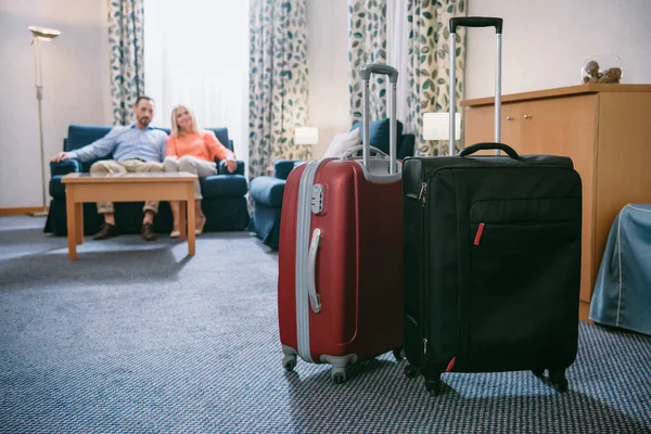 Vista de cerca de dos maletas y pareja de adultos sentados en el sofá en la habitación de hotel - foto de stock