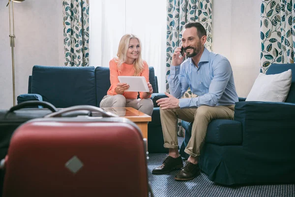 Sorrindo casal maduro usando smartphone e tablet digital enquanto sentado com malas no quarto de hotel — Fotografia de Stock