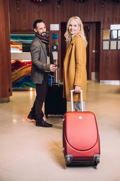 Feliz pareja madura con maletas de pie en el pasillo del hotel - foto de stock