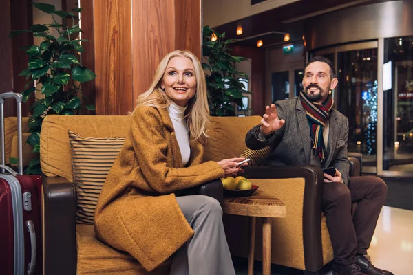 Sourire mi-adulte couple regardant loin tout en étant assis sur le couloir de l'hôtel — Photo de stock