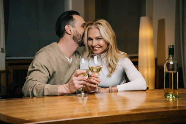 Handsome mature man whispering something to smiling woman while drinking wine in hotel restaurant — Stock Photo