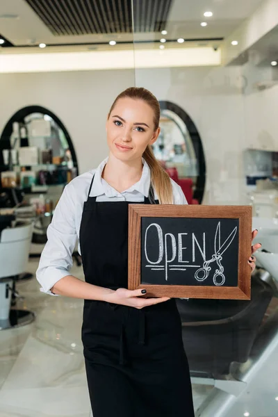 Salon de coiffure blonde souriante montrant signe ouvert — Photo de stock