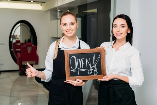 Propriétaires de salon de coiffure tenant signe ouvert et montrant pouce vers le haut — Photo de stock