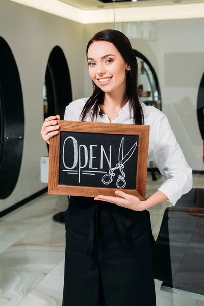 Улыбающаяся брюнетка парикмахер с открытым знаком — Stock Photo