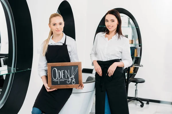 Two hairdressers with signboard open at hair salon — Stock Photo