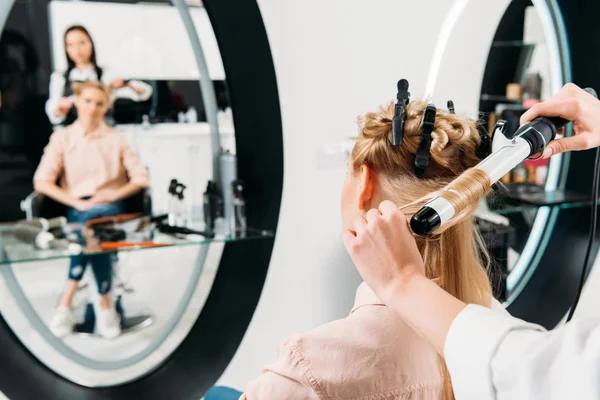 Hair stylist curling hair for customer with curling iron — Stock Photo