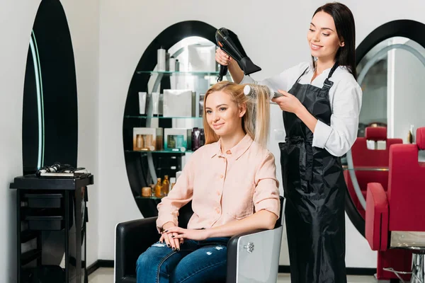Усміхнений перукар сушить волосся клієнта в салоні — стокове фото