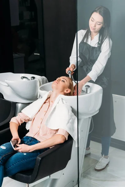 Hairdresser in apron washing customer hair — Stock Photo