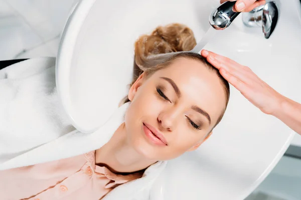 Top view of customer with closed eyes lying above washbasin while hairdresser washing hair — Stock Photo