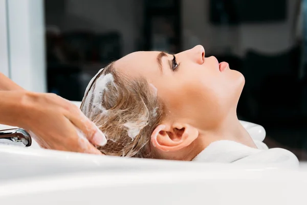 Vue latérale de coiffeur laver les cheveux pour le client avec shampooing — Photo de stock