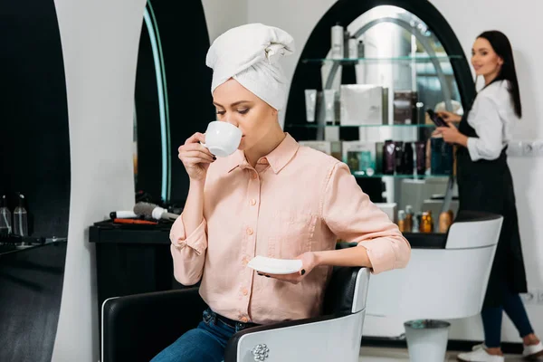 Клиент с полотенцем на голове сидя и пить кофе в парикмахерской — стоковое фото