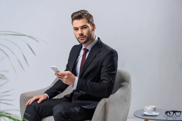 Geschäftsmann sitzt im Sessel und hält Smartphone in der Hand — Stockfoto