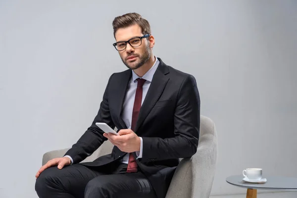 Geschäftsmann sitzt im Sessel und hält Smartphone in der Hand — Stockfoto