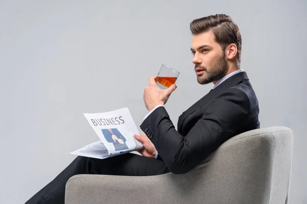 Homme d'affaires assis dans un fauteuil avec un journal et boire du whisky — Photo de stock