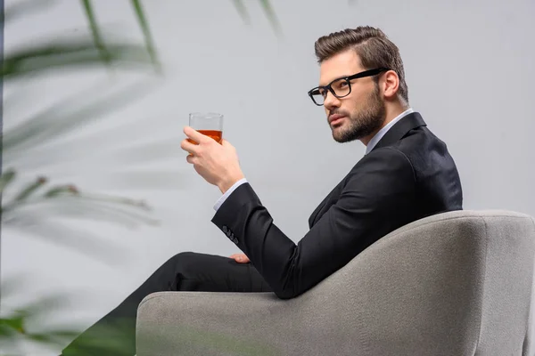 Hombre de negocios sentado en sillón con vaso de whisky - foto de stock