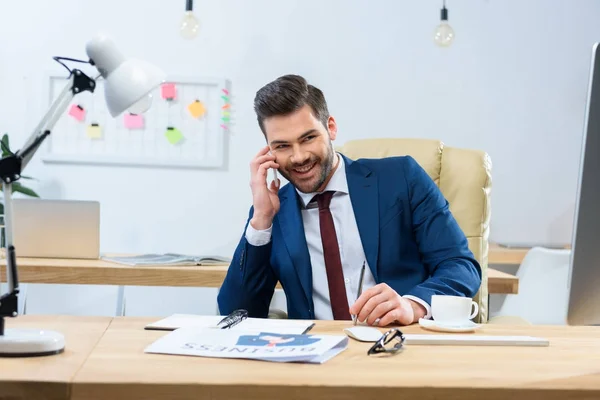 Homem de negócios bonito feliz falando por smartphone no escritório — Fotografia de Stock