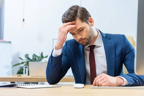 Confused businessman sitting at working table and looking down — Stock Photo