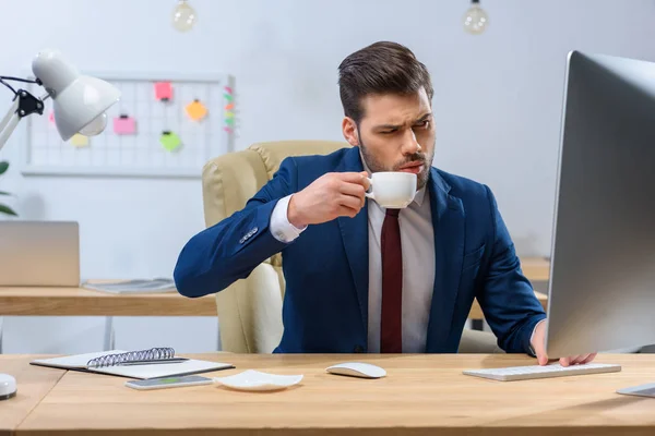 Homme d'affaires sérieux boire du café et regarder l'ordinateur — Photo de stock