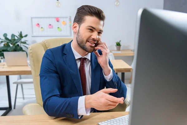 Lächelnder Geschäftsmann spricht im Büro per Smartphone — Stockfoto