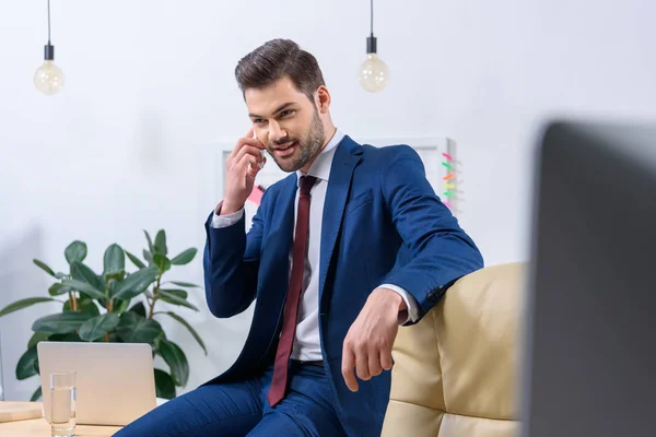 Uomo d'affari sorridente che parla tramite smartphone in ufficio — Foto stock