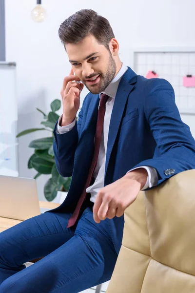 Улыбающийся бизнесмен разговаривает со смартфоном в офисе — стоковое фото