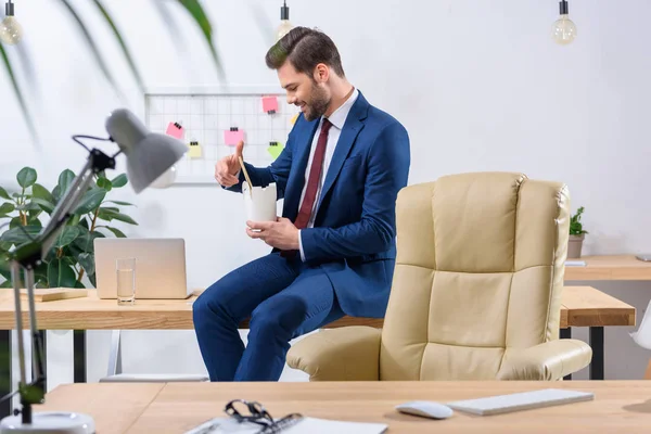 Sonriente hombre de negocios tomando fideos con palillos - foto de stock