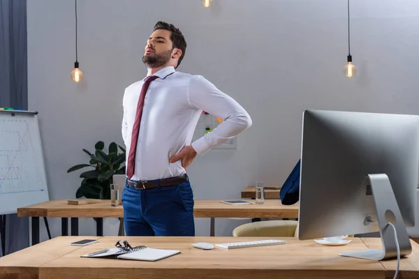 Втомлений бізнесмен стоїть і розтягується в офісі — стокове фото