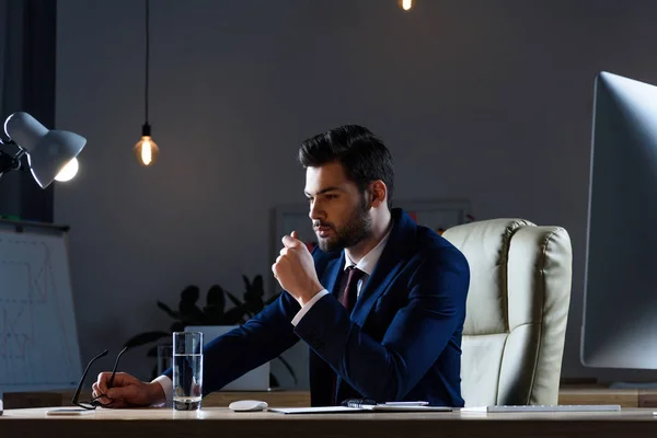 Pensativo hombre de negocios sentado en la mesa de trabajo por la noche - foto de stock