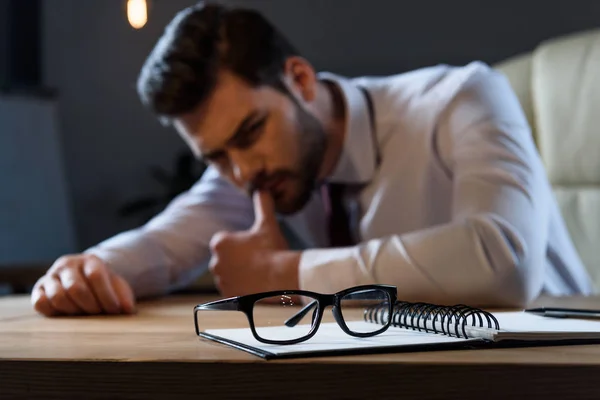 Müder, nachdenklicher Geschäftsmann lehnt am Tisch, Brille im Vordergrund — Stockfoto