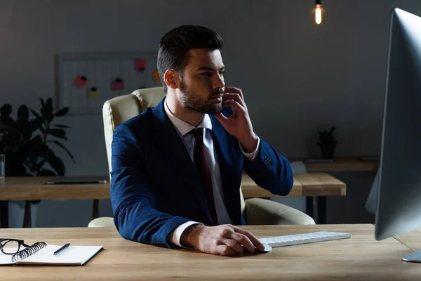 Uomo d'affari che parla con lo smartphone e utilizzando il computer — Foto stock