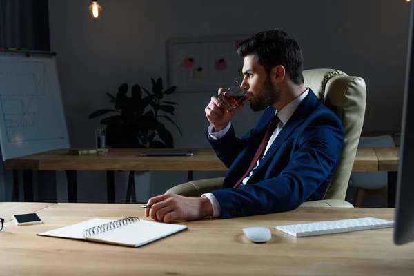Vista lateral do homem de negócios bebendo uísque no escritório escuro — Fotografia de Stock