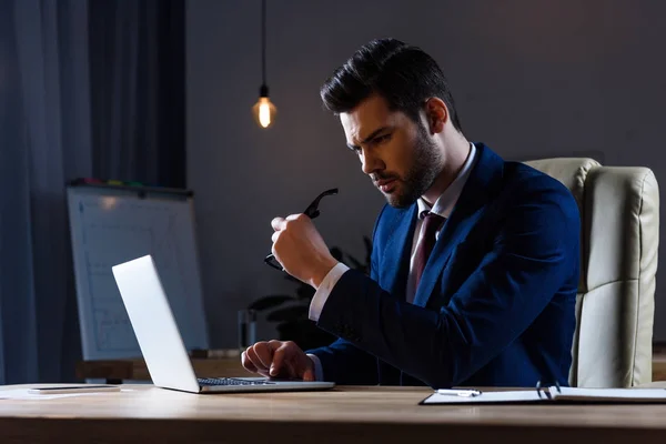 Homem de negócios sentado no escritório escuro e olhando para laptop — Fotografia de Stock