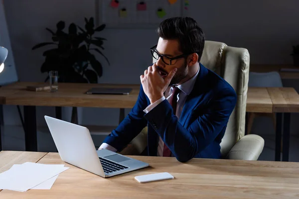 Sério homem de negócios sentado no escuro escritório e bocejo — Fotografia de Stock