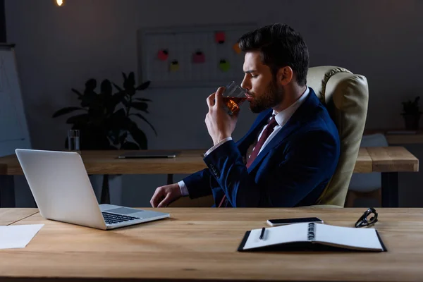 Businessman sitting in dark office and drinking whiskey — Stock Photo