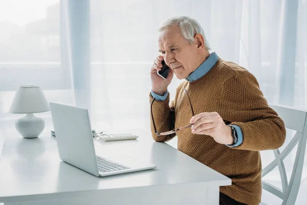 Uomo anziano occupato che lavora con il computer portatile e fa telefonate — Foto stock