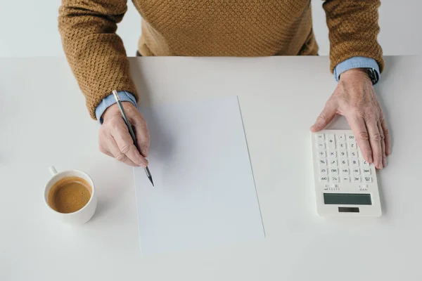 Nahaufnahme eines älteren Mannes, der auf leerem Papier schreibt und Taschenrechner benutzt — Stockfoto