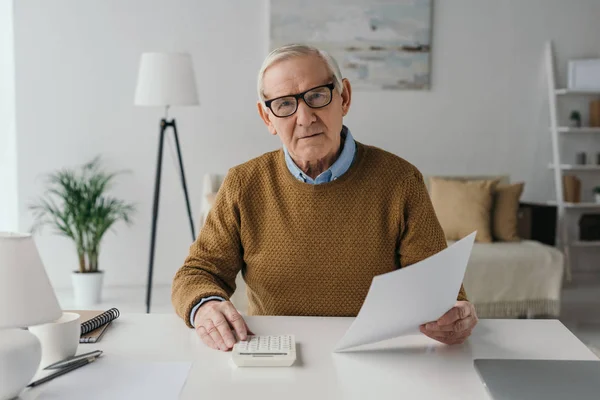 Älterer lächelnder Mann benutzt Taschenrechner und hält leeres Papier — Stockfoto