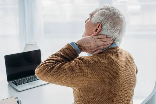 Homem mais velho trabalhando no escritório e sofrendo de dor no pescoço — Fotografia de Stock