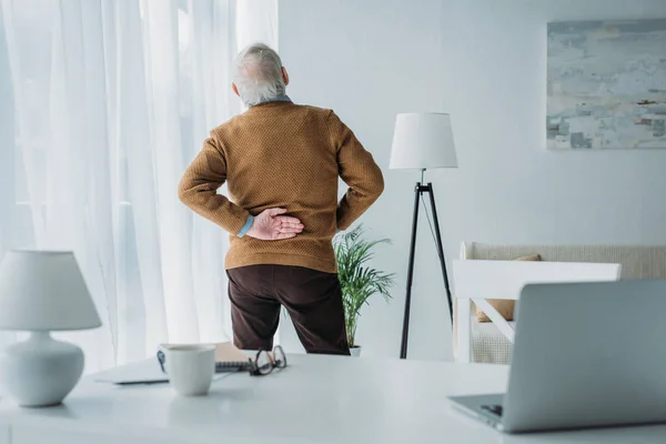 Старший мужчина страдает от болей в спине во время работы в офисе — стоковое фото