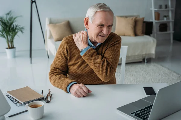 Hombre mayor que trabaja en el ordenador portátil que sufre de dolor de espalda - foto de stock