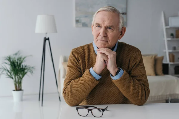 Senior thoughtful man sitting by the desk in light room — Stock Photo