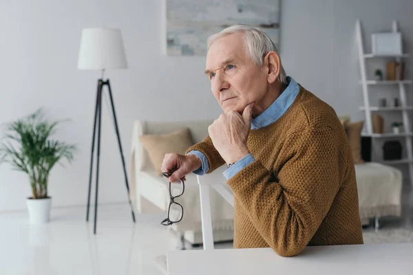 Homme âgé confiant assis près du bureau dans la salle de lumière — Photo de stock