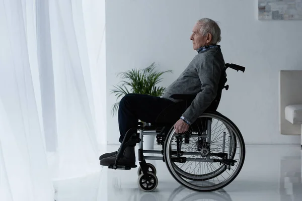 Senior thoughtful man in wheelchair looking in window — Stock Photo