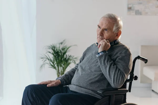 Senior hombre reflexivo en silla de ruedas en habitación vacía - foto de stock