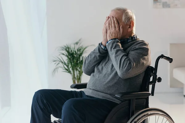 Senior triste homme en fauteuil roulant couvrant son visage avec des mains — Photo de stock