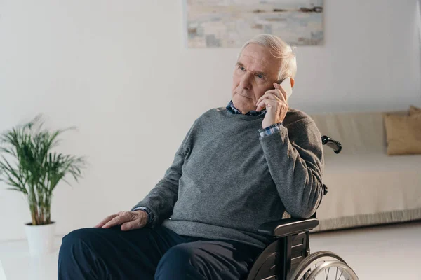 Homme âgé en fauteuil roulant faisant un appel téléphonique dans une chambre vide — Photo de stock