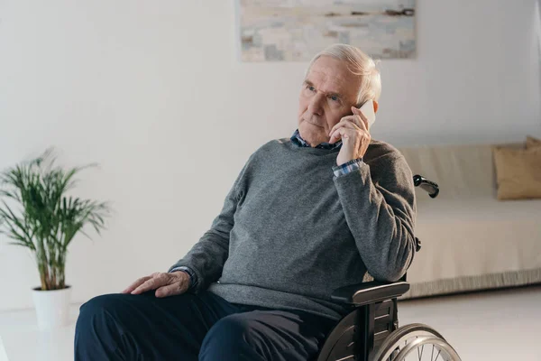 Hombre mayor en silla de ruedas haciendo una llamada telefónica en una habitación vacía - foto de stock