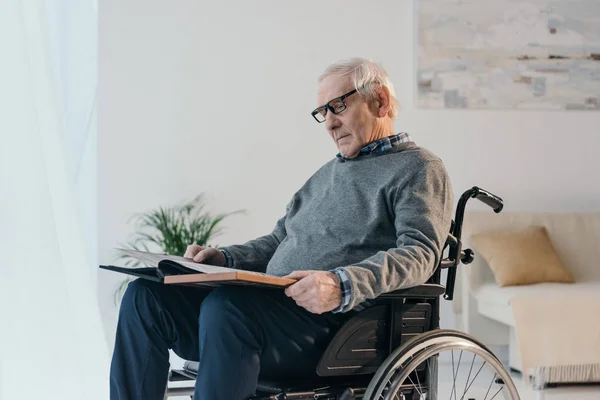 L'uomo anziano in sedia a rotelle guarda il vecchio album fotografico — Foto stock