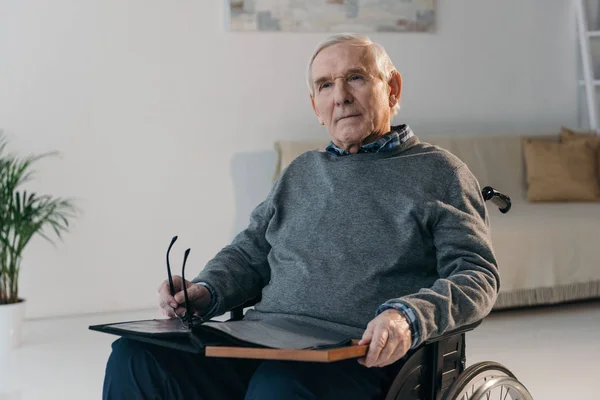 Homme âgé en fauteuil roulant tenant un vieil album photo — Photo de stock